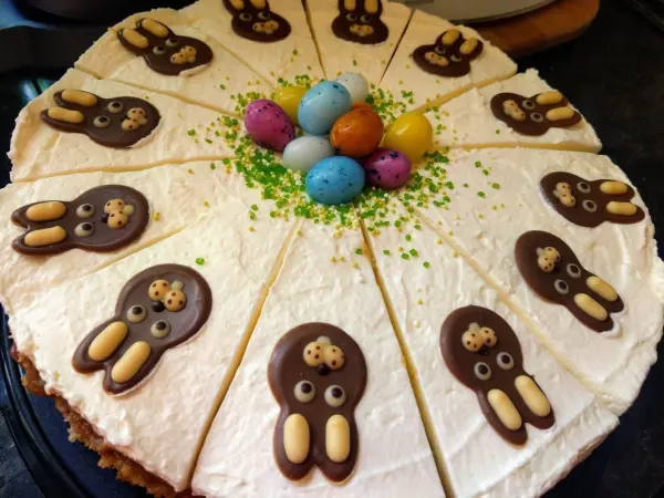 Ein Rhabarberkuchen mit bunten Schokoladenhasen und kandierten Eiern dekoriert, in einem frühlingshaften Ambiente platziert.