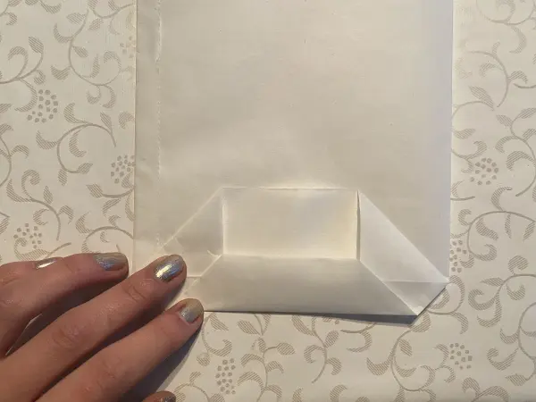 Eine Hand faltet eine leichte, transparente Lichttüte auf einem mustergedeckten Tisch, um die DIY-Idee zum Muttertag vorzubereiten.