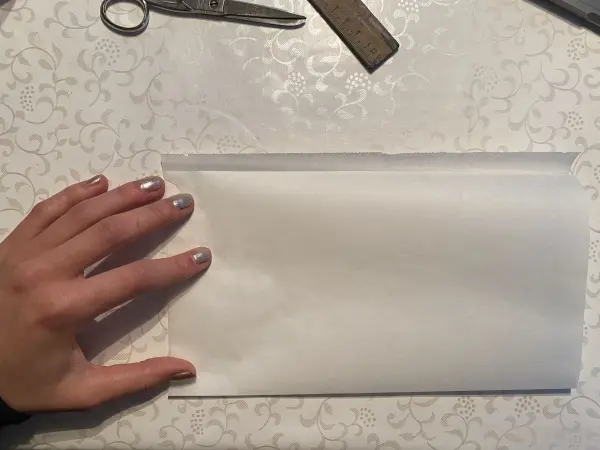 Eine Hand hält eine leere, gefaltete Tüte auf einem Tisch, um eine DIY-Lichttüte zum Muttertag zu gestalten.