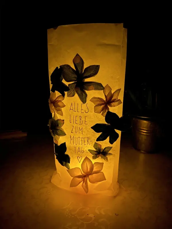 Eine lichtdurchlässige Tüte leuchtet sanft und zeigt die Botschaft „Alles Liebe zum Muttertag“ umgeben von kleinen Blumen.