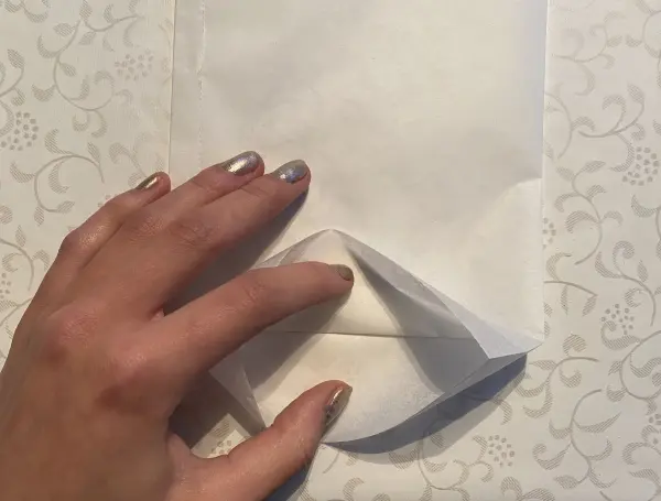 Eine Hand faltet mit Fingerspitzengefühl eine weiße Tüte, um eine Lichttüte für den Muttertag zu gestalten.