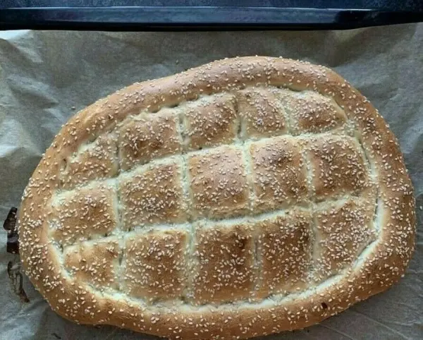Ein frisch gebackenes türkisches Fladenbrot mit Sesam liegt auf einem Backblech, umgeben von Backpapier.