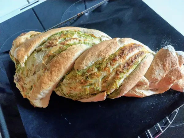Ein gezwirbeltes Käse-Kräuter-Grillbrot liegt auf einem Backblech, frisch gebacken und leicht goldbraun, bereit zum Servieren.