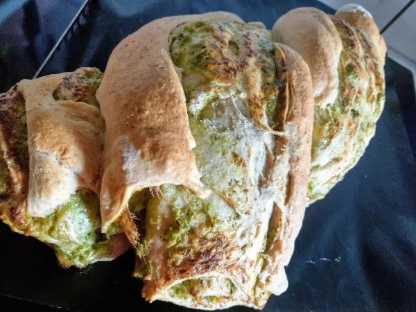 Gezwirbeltes Käse-Kräuter-Grillbrot liegt auf einem schwarzen Teller und zeigt die goldene, knusprige Kruste mit grünen Kräutern.
