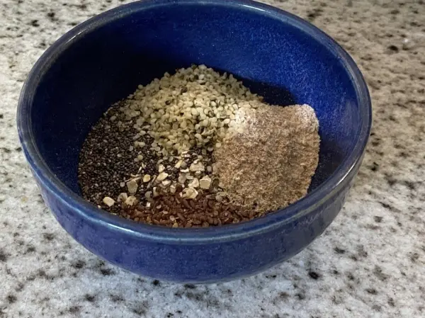 Eine blaue Schüssel enthält eine Mischung aus verschiedenen Saaten und Flocken, vorbereitet für das Power-Müsli auf einer Küchentheke.