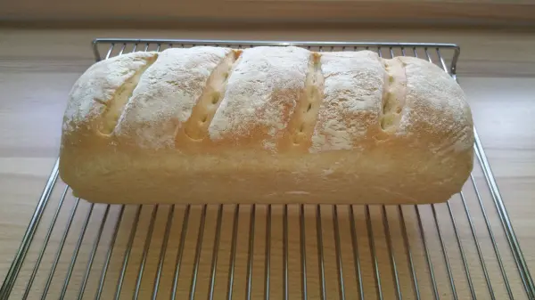 Ein frisches Toastbrot liegt auf einem Gitterrost und zeigt die goldene Kruste und typische Schnittmuster.