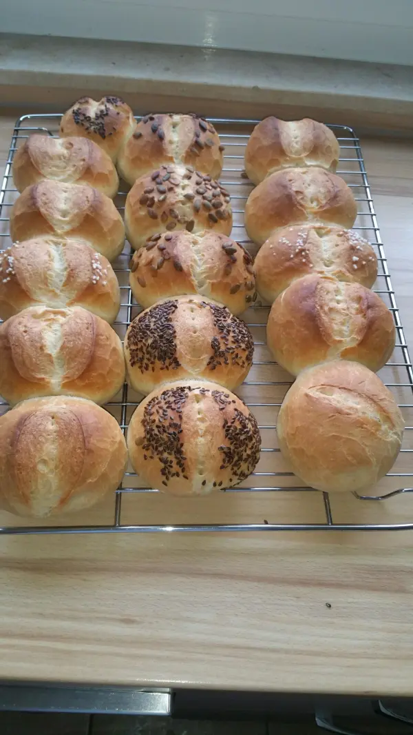 Frisch gebackene Weizenbrötchen liegen auf einem Holzgestell, goldbraun mit verschiedenen Toppings zur Dekoration.