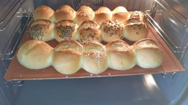 Knusprige Weizenbrötchen werden im Ofen gebacken und glänzen goldbraun auf einem Blech, umgeben von warmem Licht.