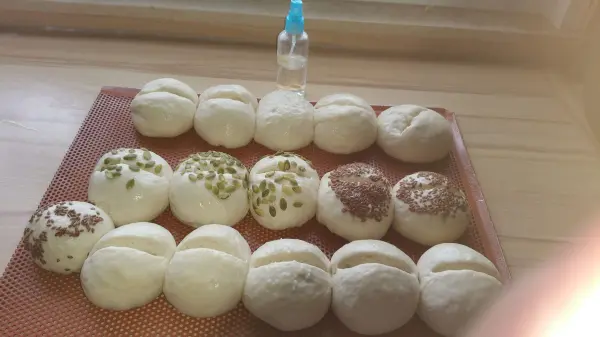 Eine Reihe von knusprigen Weizenbrötchen liegt auf einem Tablett, während ein kleiner Wasserbehälter im Hintergrund steht.