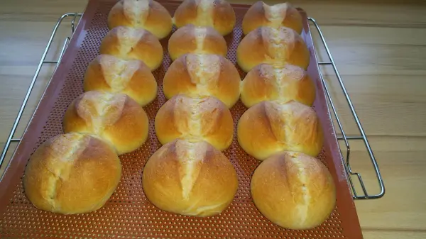 Knusprige Weizenbrötchen liegen frisch gebacken auf einem Gitter, umgeben von einer Holzoberfläche.