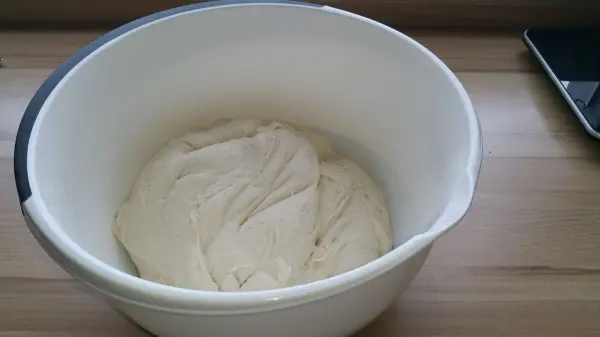 Der Teig ist in einer weißen Schüssel und ruht auf einer Holzoberfläche, bereit zum Backen von Weizenbrötchen.