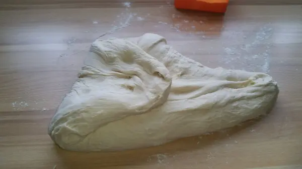Ein frischer, knuspriger Teig liegt auf einer bemehlten Arbeitsfläche und wartet darauf, zu Weizenbrötchen geformt zu werden.