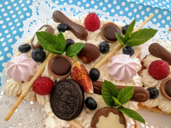 Ein einzigartiger Number Cake mit frischen Früchten und Schokolade liegt auf einem blauen, gepunkteten Tischtuch.