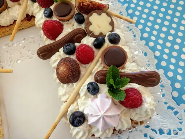 Ein aufwändiger Number Cake mit Sahne, Früchten und Süßigkeiten ist auf einem Tisch in einer bunten, gepunkteten Umgebung platziert.