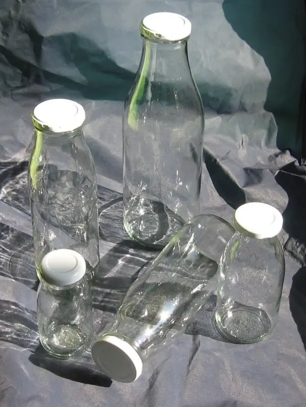 Glasflaschen stehen chaotisch auf einem grauen Untergrund, bereit fürs herbstliche Dekorieren mit Naturmaterialien.