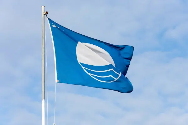 Eine blaue Flagge weht am Mast, während der Himmel klar ist. Sie symbolisiert die Ostsee und zieht Aufmerksamkeit auf Warnemünde.