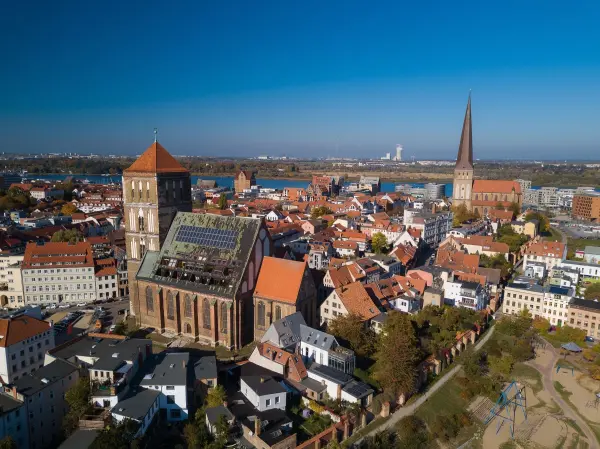 Die Ostsee erstreckt sich über eine malerische Stadt mit historischen Gebäuden und bunten Dächern bei strahlend blauem Himmel.