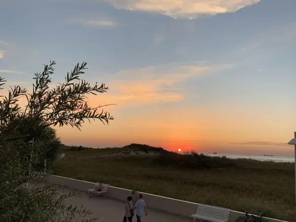 Eine malerische Küstenlandschaft bei Sonnenuntergang, mit zwei Personen, die am Strand entlang spazieren.
