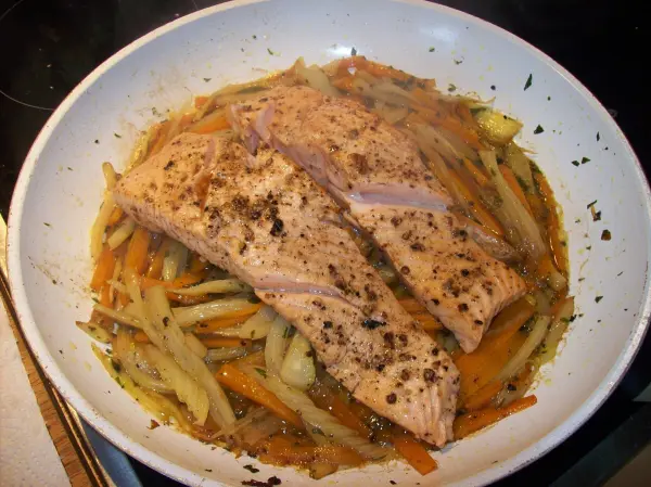 Zart gegrillter Lachs liegt auf einem bunten Gemüse aus Fenchel und Möhren in einer weißen Schüssel.