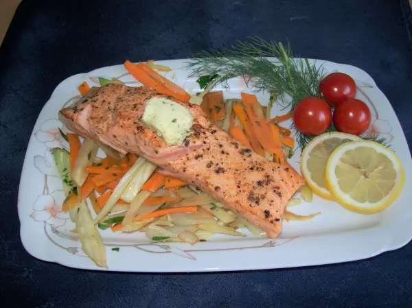 Zarter Lachs liegt auf buntem Fenchel-Möhren-Gemüse, garniert mit Dill, Zitrone und Kirschtomaten auf einem Teller.