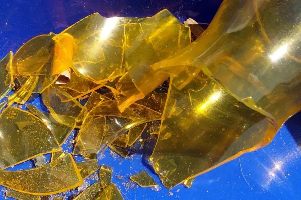 Zersplitterte Glasreste liegen auf einem blauen Untergrund, nachdem eine volle Flasche heruntergefallen ist.