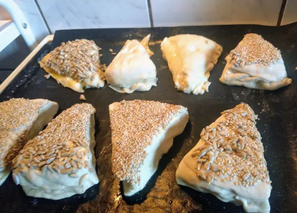 Auf einem Backblech liegen mehrere Laugendreiecke, goldbraun gebacken und mit Sesam bestreut. Sie sind frisch aus dem Ofen.