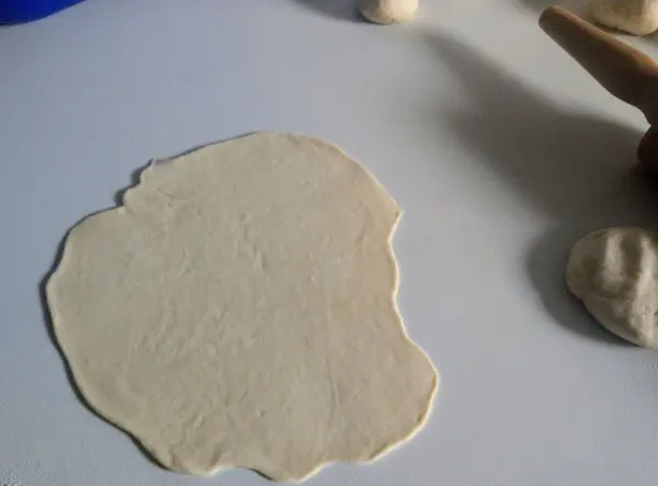 Ein flacher Teigling liegt auf einer Arbeitsfläche, während im Hintergrund weitere Teigstücke bereit stehen. Laugendreiecke selbst gemacht.