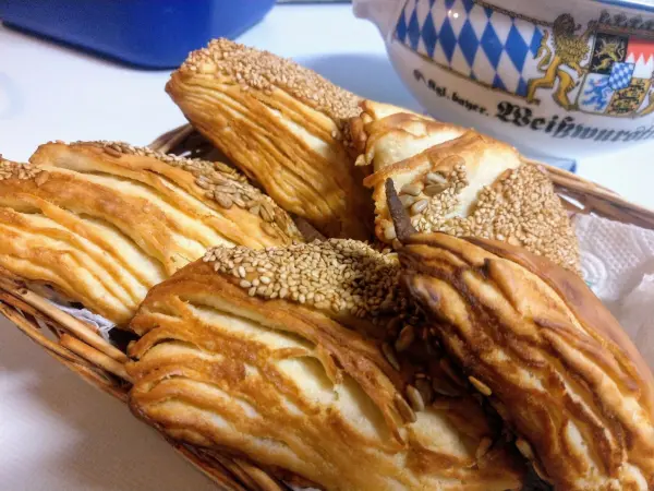 Flaky Laugendreiecke sind in einem Korb angeordnet, umgeben von einer hellen Tischoberfläche und einem bayerischen Geschirr.