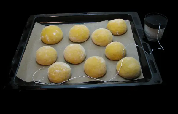 Frisch geformte Kürbisbrötchen liegen auf einem Backblech, bereit zum Backen in einer dunklen Umgebung.