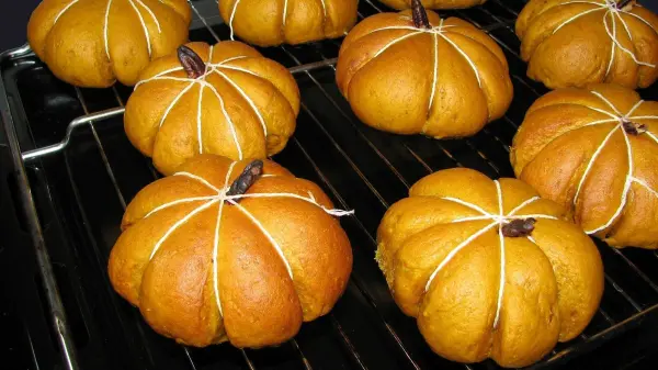 Kürbisbrötchen liegen frisch auf einem Rost und zeigen ihre runde, orange Farbe in einer gemütlichen Küche.