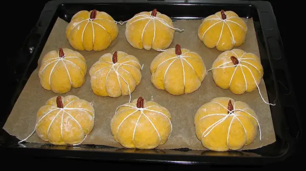 Kürbisbrötchen in Form von kleinen Kürbissen stehen frisch auf einem Backblech, bereit zum Backen in der Küche.