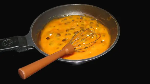 Eine Pfanne mit Kürbisbrötchen-Teig, der mit einem Schneebesen rührt, befindet sich vor einem dunklen Hintergrund.