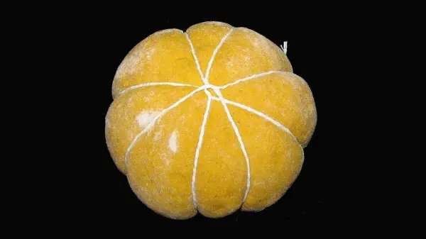 Ein gelbes Kürbisbrötchen liegt auf einem schwarzen Hintergrund und strahlt durch seine runde Form und die feine Garnierung.