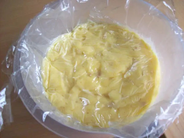 Eine Schüssel mit einer cremigen Füllung, bedeckt mit Frischhaltefolie, wartet auf die Zubereitung von Pasteis de Belem.