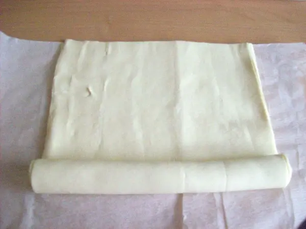 Ein aufgerollter Blätterteig liegt auf einer Fläche aus Backpapier, bereit zum Füllen für Pasteis de Belem.