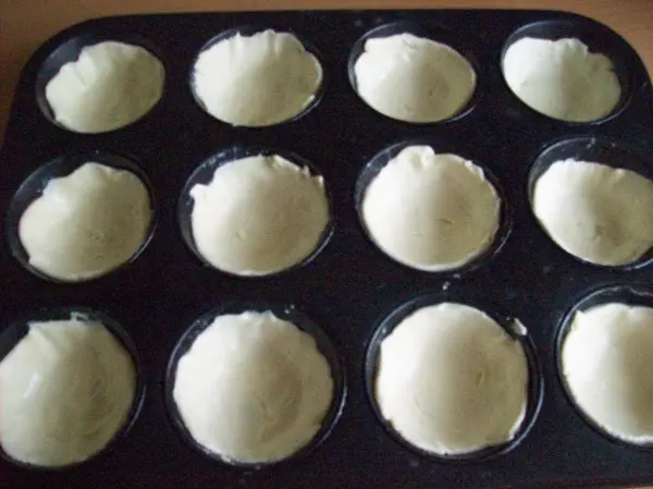 Kleine, runde Teigportionen in einer Muffinform sind bereit, im Ofen gebacken zu werden, um Pasteis de Belem zu werden.