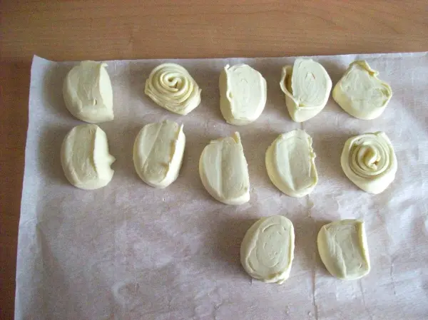 Auf einem Backpapier liegen mehrere kleine, vorgeformte Teigstücke, die für die Zubereitung von Pasteis de Belem bereit sind.