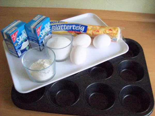 Zutaten für Pasteis de Belem sind auf einem Tablett arrangiert, bereit zum Backen in einem Muffinblech.