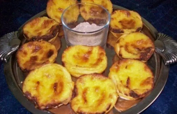 Zarte Pasteis de Belem sind auf einem silbernen Tablett angerichtet, umgeben von einer Schüssel mit Zucker.