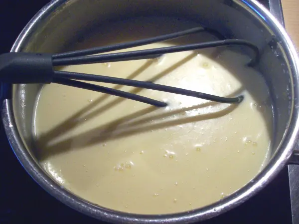 Eine Schüssel mit einer cremigen Mischung wird mit einem Schneebesen gerührt, ideal für die Zubereitung von Pasteis de Belem.