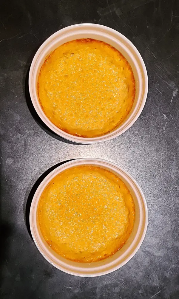 Zwei goldbraune Pasteis de Belem liegen in weißen Schalen auf einer dunklen Oberfläche, bereit zum Genießen.