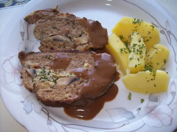 Ein gefüllter Hase aus Hackfleisch, mit Kräutern und Champignons, liegt auf einem Teller neben Kartoffeln.