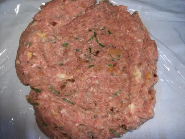 Ein gefüllter Falscher Hase liegt auf einer hellen Unterlage, bereit zum Kochen, gefüllt mit Kräutern und Champignons.