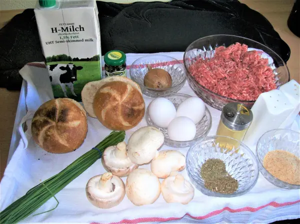 Auf einem Tisch liegen Zutaten für einen Falschen Hasen: Quellmilch, Hackfleisch, Eier, Kräuter und Champignons.