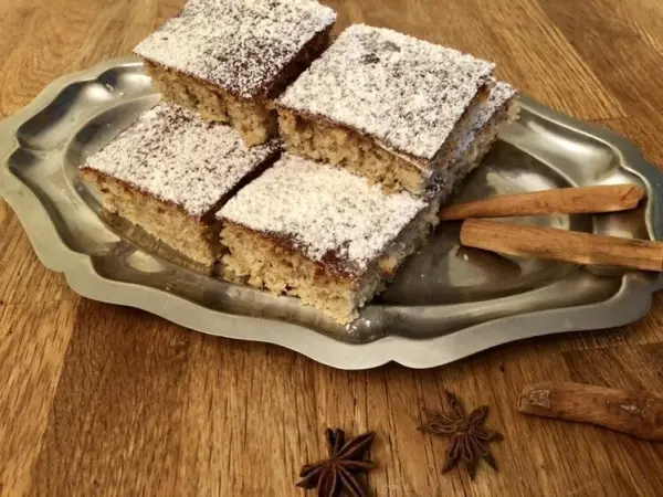 Ein platter Lebkuchen-Kuchen ist auf einem Silbertablett angeordnet, bestäubt mit Puderzucker und umgeben von Zimtstangen.