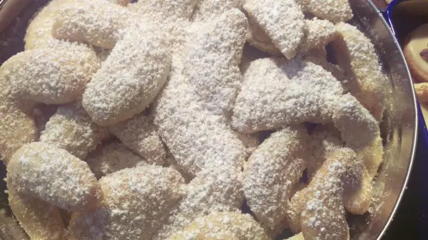 Leckere Vanillekipferl liegen auf einem silbernen Teller, bestäubt mit Puderzucker, in einer gemütlichen Küchenszene.