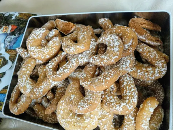 Plätzchen aus Vanillekipferl liegen in einer Dose, staubzuckerbestäubt, bereit zum Genießen in einer festlichen Umgebung.
