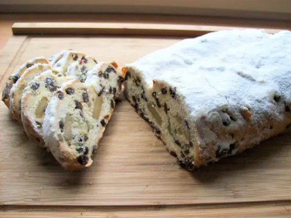 Saftiger Christstollen mit Marzipan liegt auf einem Holzbrett, während eine Scheibe herausgeschnitten wurde, um die Füllung zu zeigen.