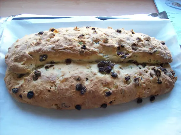 Ein frisch gebackener Christstollen mit Marzipan, auf einem Blech liegend, geschmückt mit Rosinen und Puderzucker.