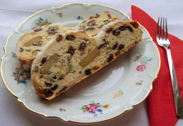 Auf einem eleganten, blumenverzierten Teller liegen zwei Scheiben von Christstollen mit Marzipan und Trockenfrüchten.